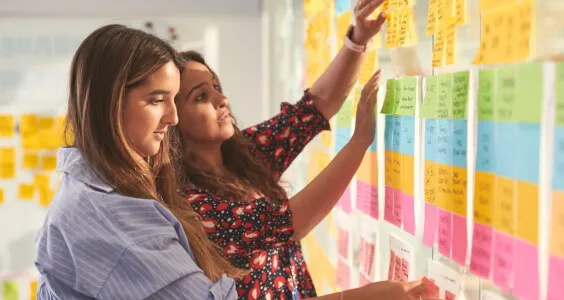 Side view of two female colleagues arranging sticky notes on a glass wall