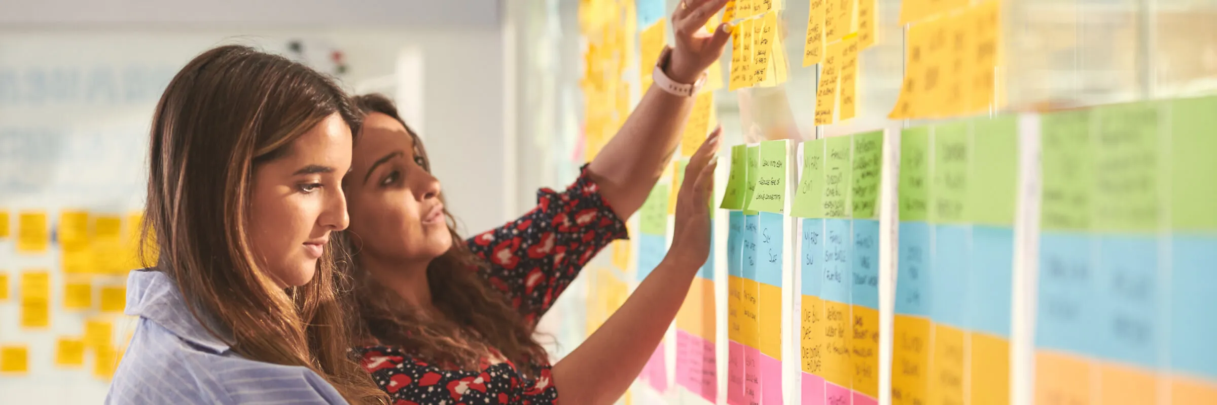 Side view of two female colleagues arranging sticky notes on a glass wall