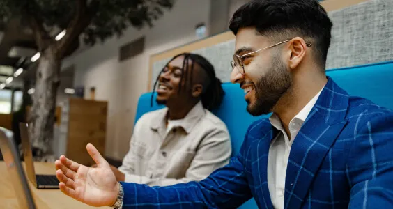 Side view of young asian man wearing a suit and glasses gesturing whilst talking to colleagues