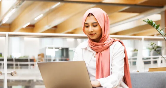 Young asian woman wearing head scarf working at a laptop in modern office