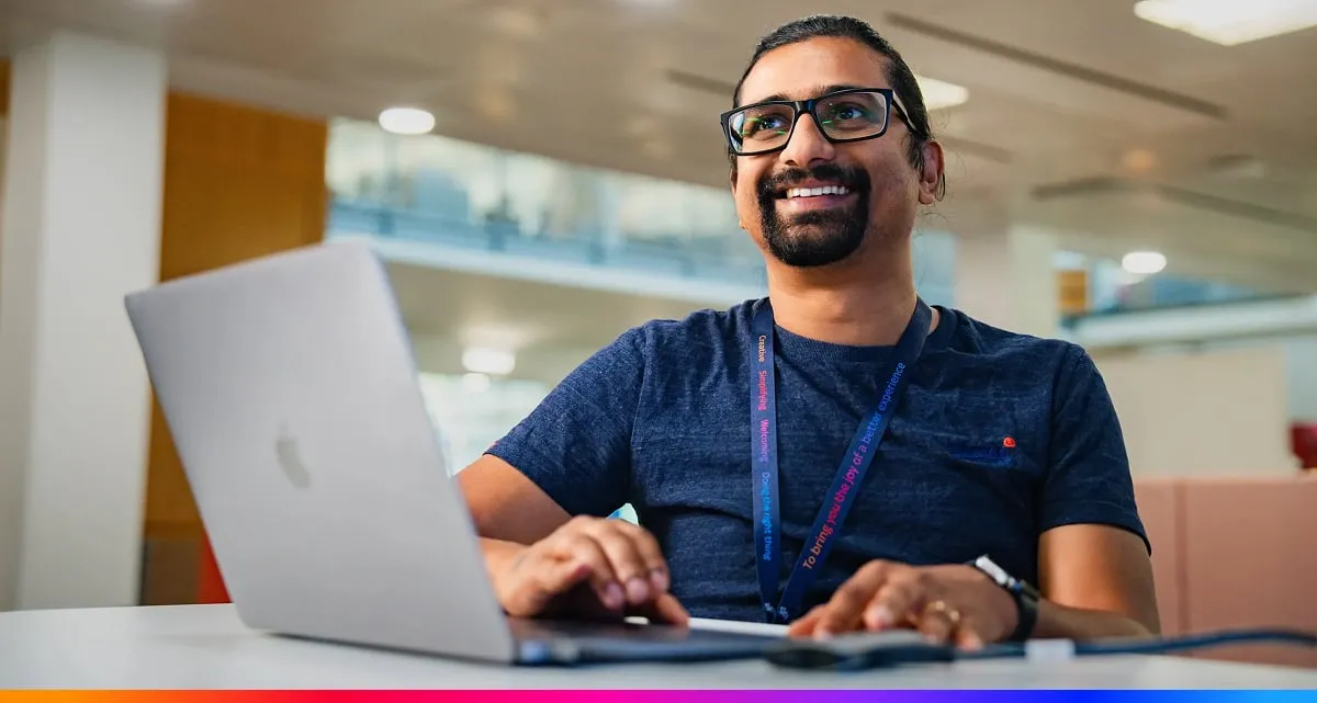 A Smiling Man With Glasses Types on a Laptop at a Desk in a Bright Modern Office